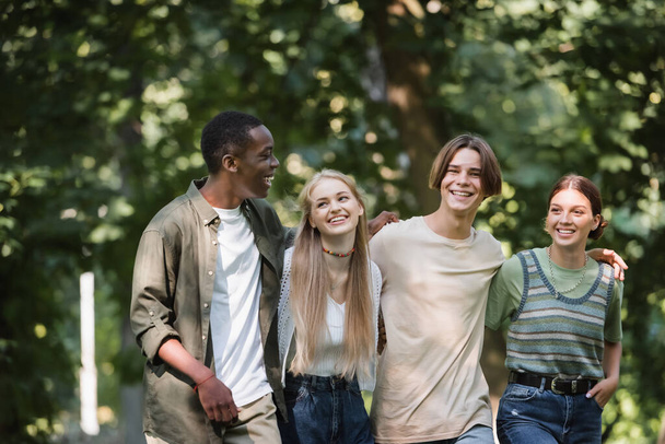 Cheerful multiethnic teenagers embracing in park  - Фото, изображение