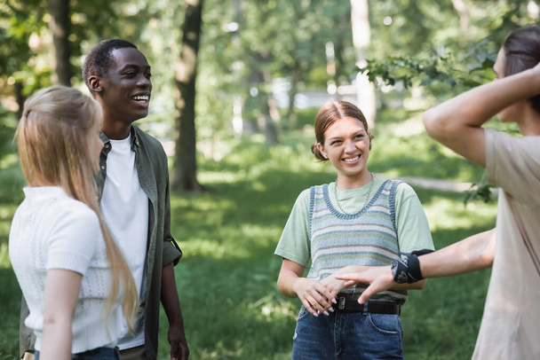 Smiling interracial teenagers looking at blurred friend in park  - Fotó, kép
