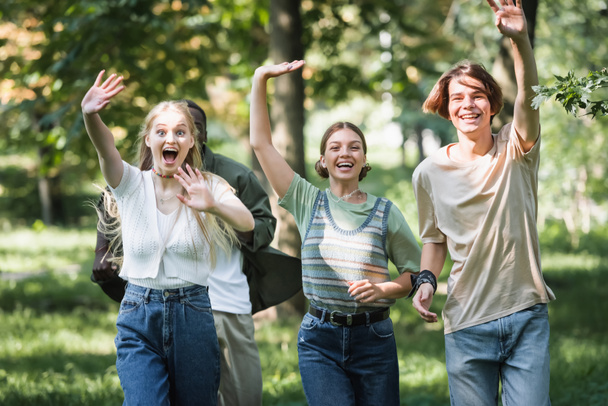 Happy interracial teenagers waving hands at camera in park  - Photo, Image