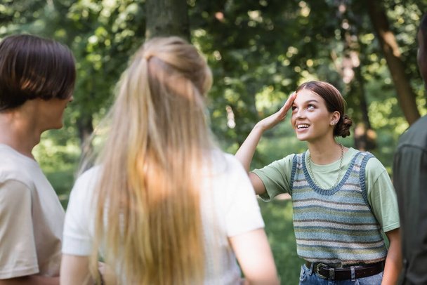 Smiling teenage girl standing near blurred interracial friends outdoors - Foto, imagen