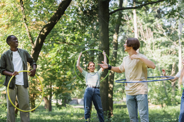 Teen boy with hula hoop pointing at african american friend in park  - Fotografie, Obrázek