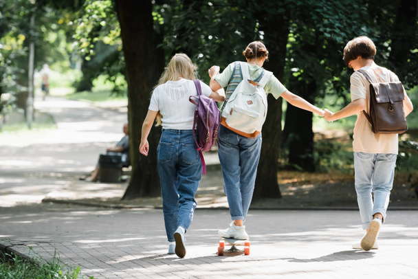 Teen boy holding hand of friend on skateboard in park  - Photo, image