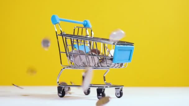 Geld Munten vallen in speelgoed supermarkt kar of trolley geïsoleerd op felgele achtergrond. Veilig online winkelen of verkoop concept. Full HD slow motion video - Video