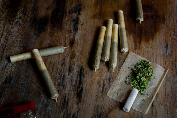 A close up shot of rolled up joints with green cannabis, lighter and paper. - Photo, Image