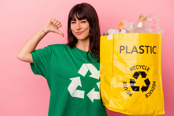 Joven mujer caucásica sosteniendo una bolsa de plástico reciclado aislado sobre fondo rosa se siente orgulloso y seguro de sí mismo, ejemplo a seguir. - Foto, imagen