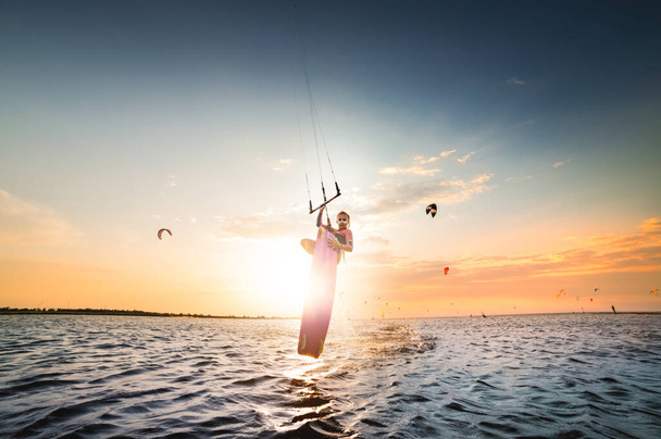 Young caucasian woman kitesurfer doing a jump trick on a sunset background. The girl hides the setting sun in a jump. double-sided copy space. Central composition. Kitesurfer spot - Foto, imagen
