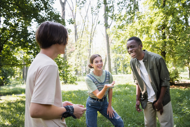 Adolescente sonriente señalando a un amigo afroamericano en el parque  - Foto, Imagen