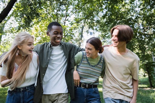 Interracial tizenévesek mosolyognak és ölelkeznek a parkban  - Fotó, kép