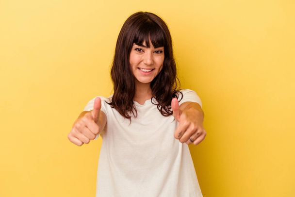 Fiatal fehér nő elszigetelt sárga háttér emeli mindkét hüvelykujját fel, mosolygós és magabiztos. - Fotó, kép