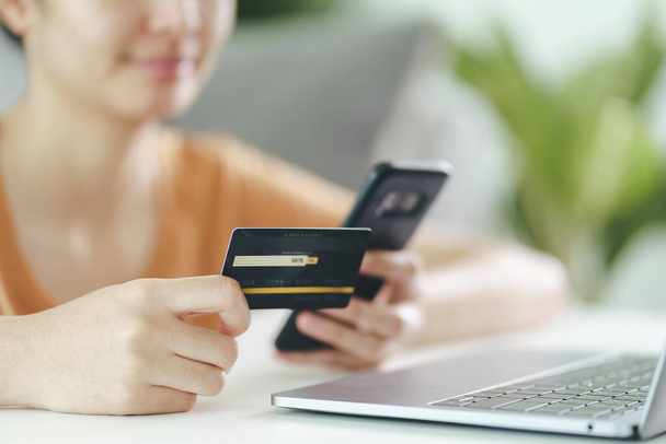 Young woman holding credit card and using smart phone for online shopping, internet banking, e-commerce, spending money, working from home concept - Photo, Image