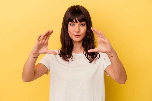 Young caucasian woman isolated on yellow background holding something with palms, offering to camera. - Photo, image