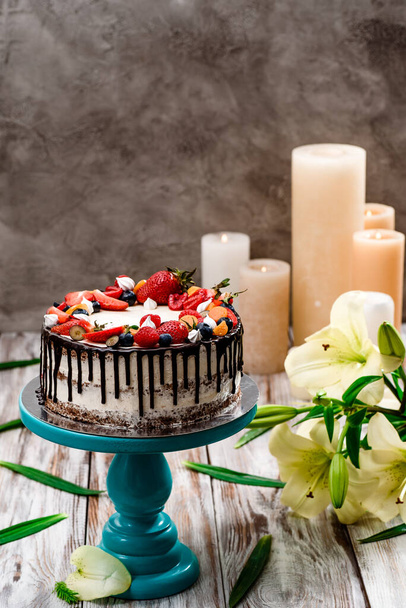 Beautiful cake with fresh berries and chocolate drops on a cake stand on a white wooden background. Space for text - Photo, Image