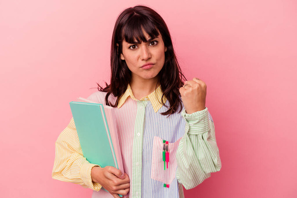Jovem estudante caucasiana segurando livros isolados em fundo rosa mostrando punho para câmera, expressão facial agressiva. - Foto, Imagem