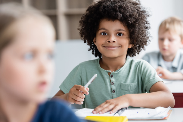 african american kid smiling at camera near blurred classmates - Foto, Imagen