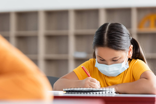 asiatico studentessa in medico maschera scrittura in notebook in aula - Foto, immagini