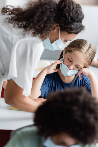 Afrykański amerykański nauczyciel w masce medycznej pomaga dziewczynie podczas lekcji - Zdjęcie, obraz