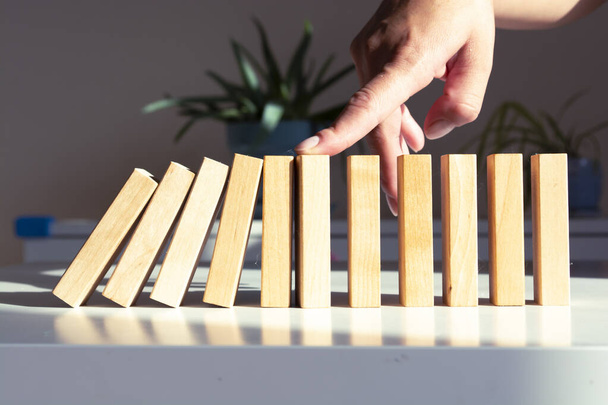 partial view of woman sitting at desk and preventing wooden blocks from falling with hand - Photo, Image