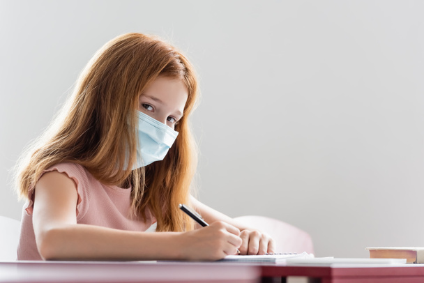 schoolgirl in medical mask writing during school lesson - Zdjęcie, obraz