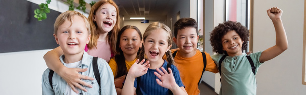 nadšení multietničtí spolužáci mávající rukama a předvádějící radostné gesto ve školním sále, prapor - Fotografie, Obrázek