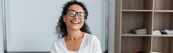 joyful african american teacher in eyeglasses smiling in classroom, banner - Photo, Image