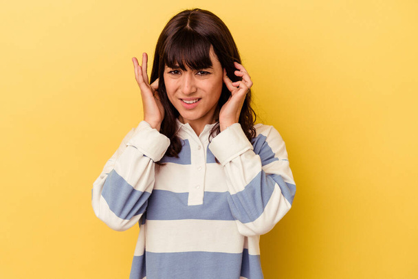 Young caucasian woman isolated on yellow background covering ears with fingers, stressed and desperate by a loudly ambient. - Foto, afbeelding