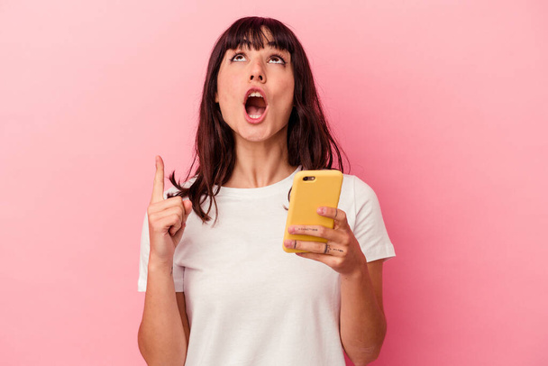 Joven mujer caucásica sosteniendo un teléfono móvil aislado sobre fondo rosa apuntando al revés con la boca abierta. - Foto, Imagen