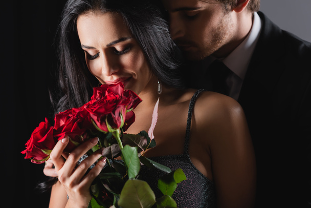 усміхнена жінка тримає троянди біля хлопця на чорному
  - Фото, зображення