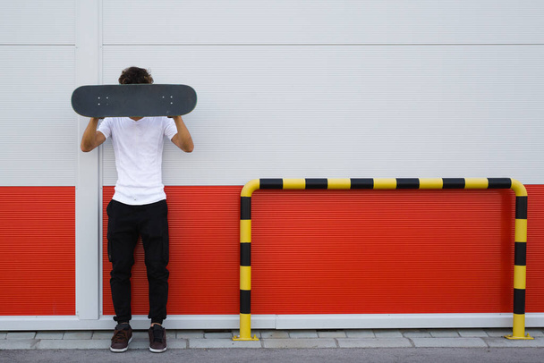 skateboarder posing against red and white wall - Foto, afbeelding