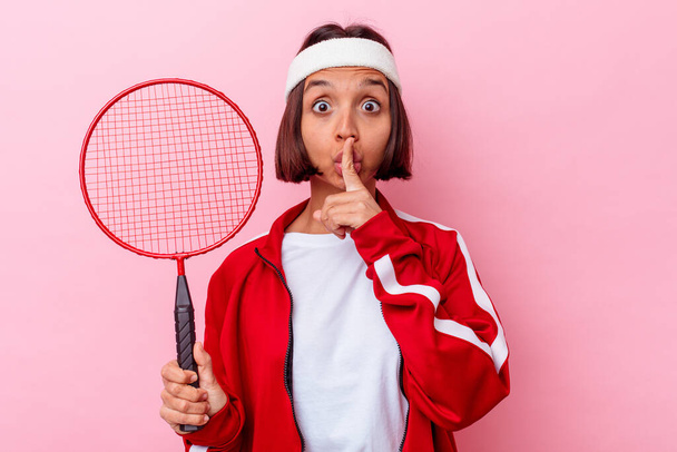 Young mixed race woman playing badminton isolated on pink background keeping a secret or asking for silence. - Photo, Image