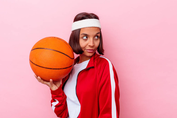 Genç melez bir kadın pembe arka planda izole edilmiş basketbol oynuyor. Gülümsüyor, neşeli ve keyifli.. - Fotoğraf, Görsel
