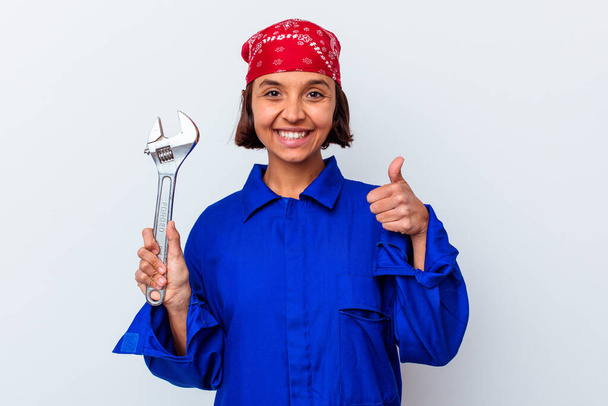 Mujer mecánica joven sosteniendo una llave aislada sonriendo y levantando el pulgar hacia arriba - Foto, imagen