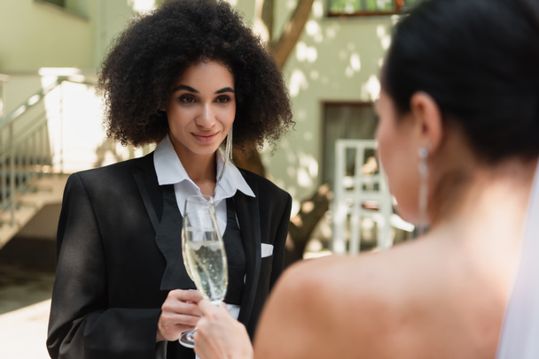 African american lesbian woman toasting champagne with blurred girlfriend during wedding outdoors - Foto, Imagem