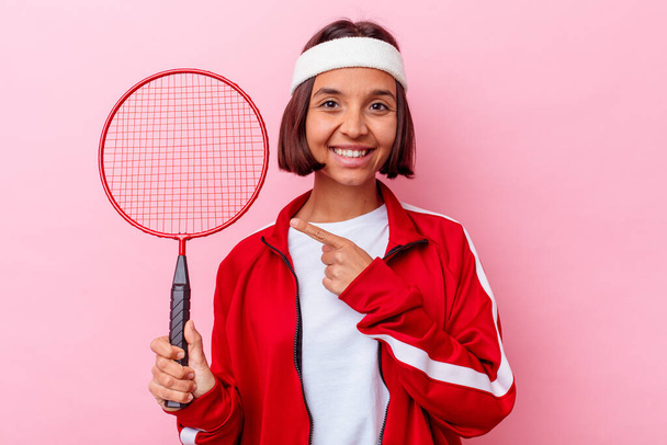 Młoda mieszana rasa kobieta gra badminton odizolowany na różowym tle uśmiechając się i wskazując na bok, pokazując coś w pustej przestrzeni. - Zdjęcie, obraz