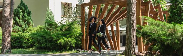 Pareja multiétnica del mismo sexo con ramo de bodas caminando en el parque, pancarta  - Foto, imagen