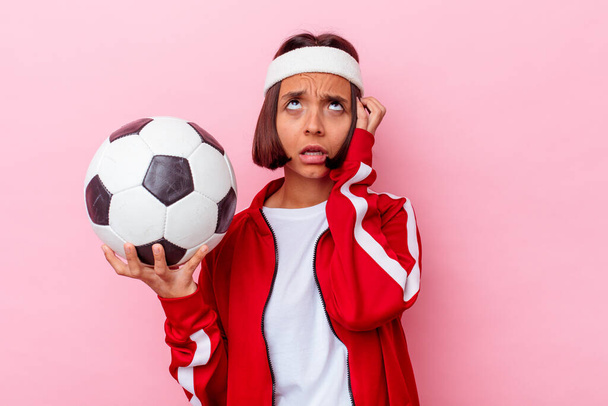 Nuori sekarotuinen nainen pelaa jalkapalloa eristetty vaaleanpunainen tausta on järkyttynyt, hän on muistanut tärkeä kokous. - Valokuva, kuva