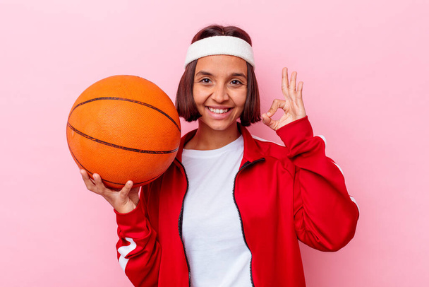 Basketbol oynayan genç melez kadın pembe arka planda izole edilmiş neşeli ve kendinden emin.. - Fotoğraf, Görsel