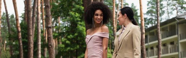 Veselý interracial lesbičky pár ve formálním oblečení při pohledu na sebe v parku, banner  - Fotografie, Obrázek
