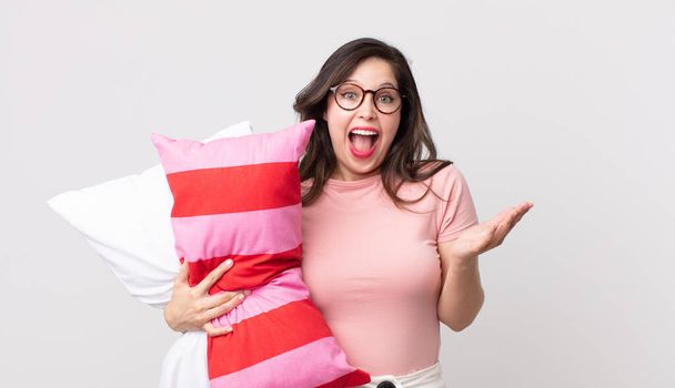 pretty woman feeling happy and astonished at something unbelievable wearing pajamas and holding a pillow - Photo, image