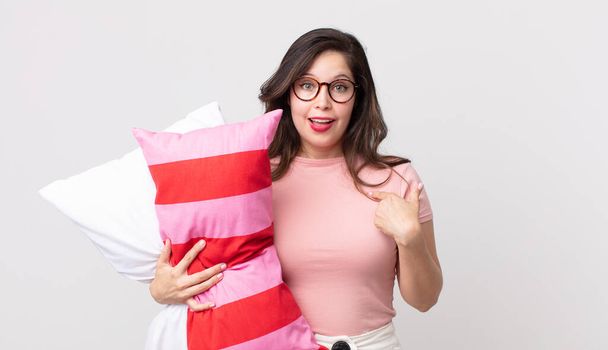 pretty woman feeling happy and pointing to self with an excited wearing pajamas and holding a pillow - Photo, image