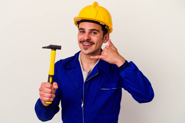 Junger kaukasischer Arbeiter mit einem Hammer auf weißem Hintergrund, der eine Handygeste mit den Fingern zeigt. - Foto, Bild