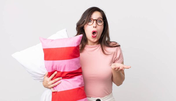 pretty woman feeling extremely shocked and surprised wearing pajamas and holding a pillow - Photo, Image