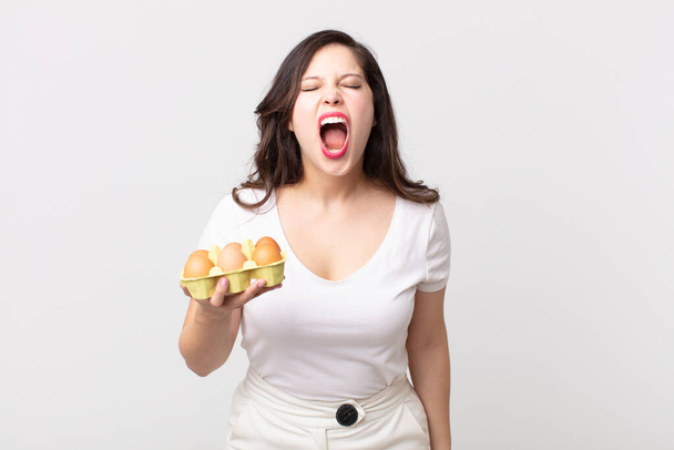 pretty woman shouting aggressively, looking very angry and holding an eggs box - Fotoğraf, Görsel