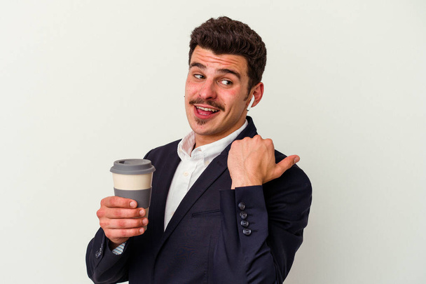 Young business caucasian man wearing wireless headphones and holding take way coffee isolated on white background points with thumb finger away, laughing and carefree. - Foto, Bild