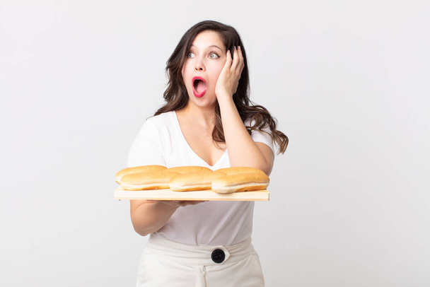 pretty woman feeling happy, excited and surprised and holding a bread roll tray - Foto, Imagen