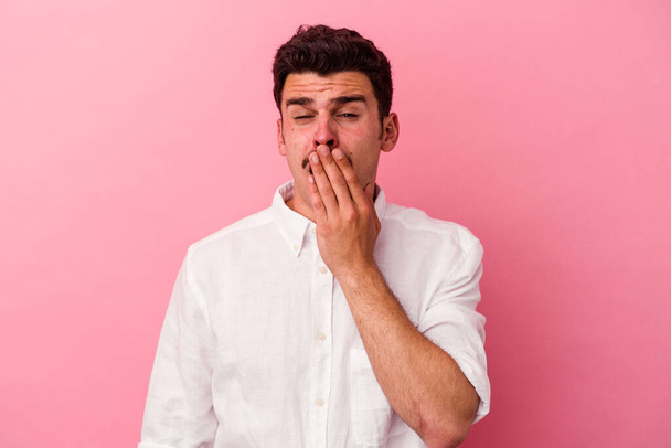 Jonge blanke man geïsoleerd op roze achtergrond geeuwen tonen een moe gebaar bedekken mond met de hand. - Foto, afbeelding