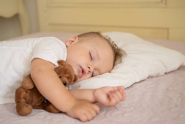 家でベッドで寝てる面白い赤ちゃん。テディベアを抱いた子供は - 写真・画像