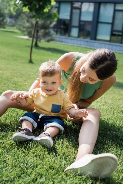 young mother sitting on grass with happy toddler son outside  - Фото, зображення