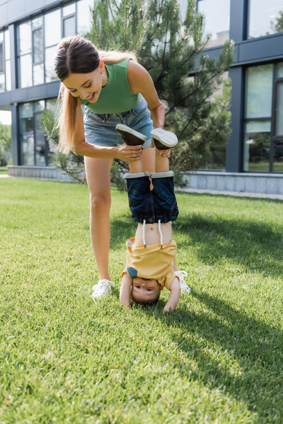 full length of happy mother supporting toddler son doing handstand  - Fotografie, Obrázek