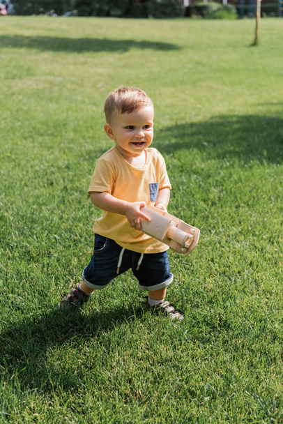 cheerful toddler boy with toy wooden car while walking on grass - Photo, Image