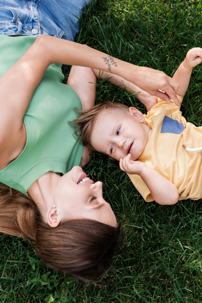 top view of cheerful mother spending time with happy toddler son while lying on grass  - Photo, image